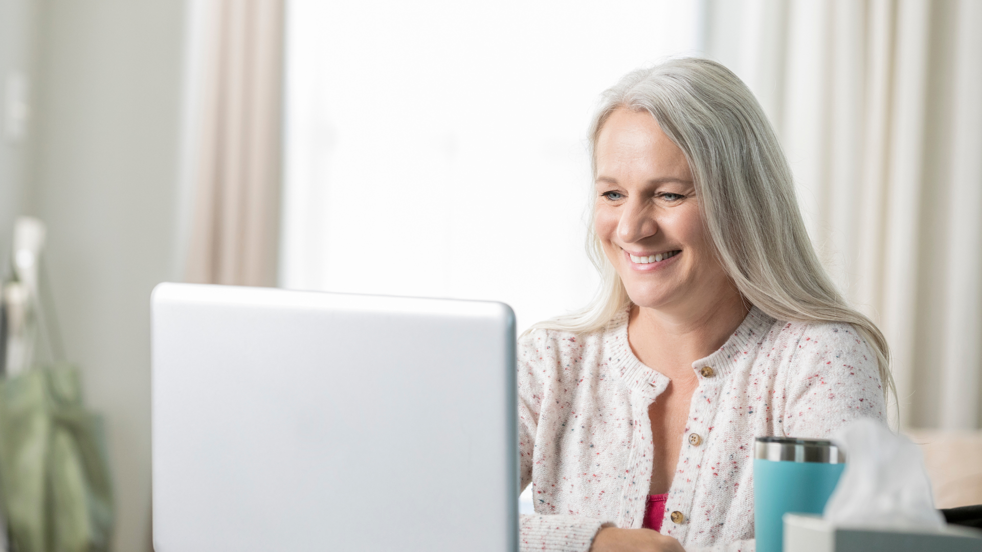 Smiling woman using a laptop at home, representing the convenience of telehealth and virtual consultations.